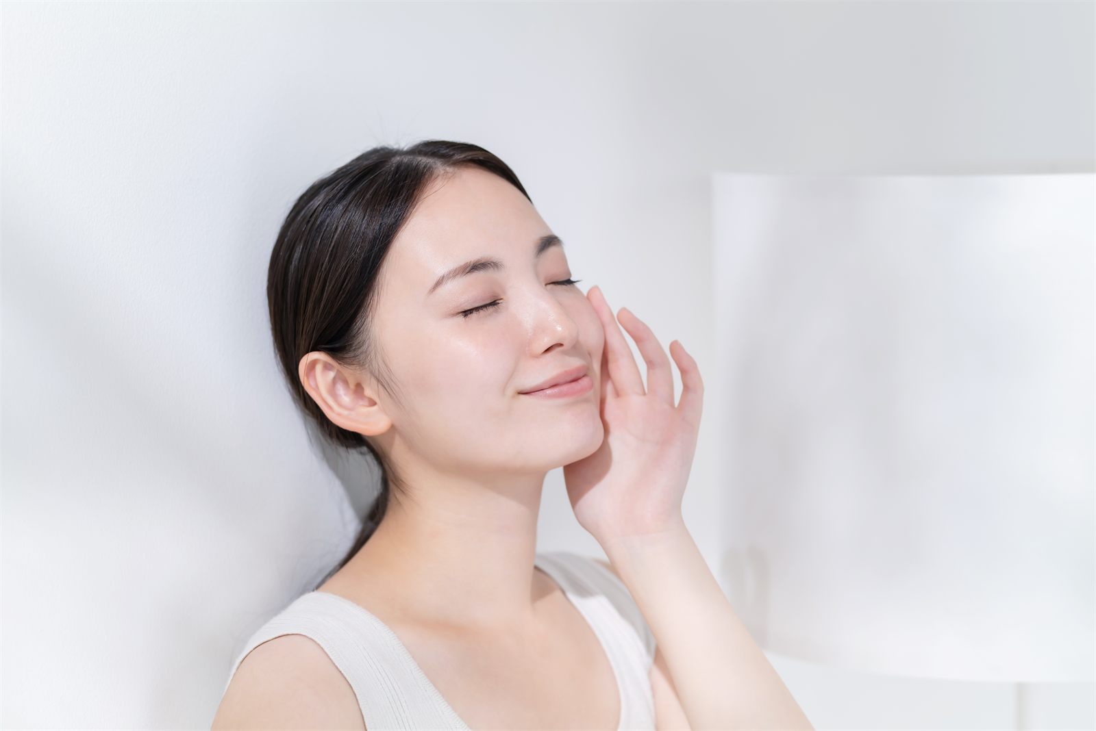 明るい光のなかで、頬にそっと手を添える女性